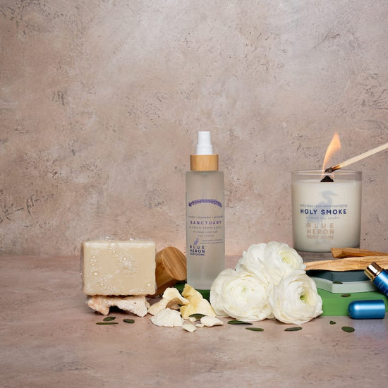 Collection of bath and body products including a candle, soap, room spray and inhaler on a textured surface.