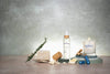 Collection of wellness products including a candle, bottle, and stones on a wooden surface with a concrete wall background.