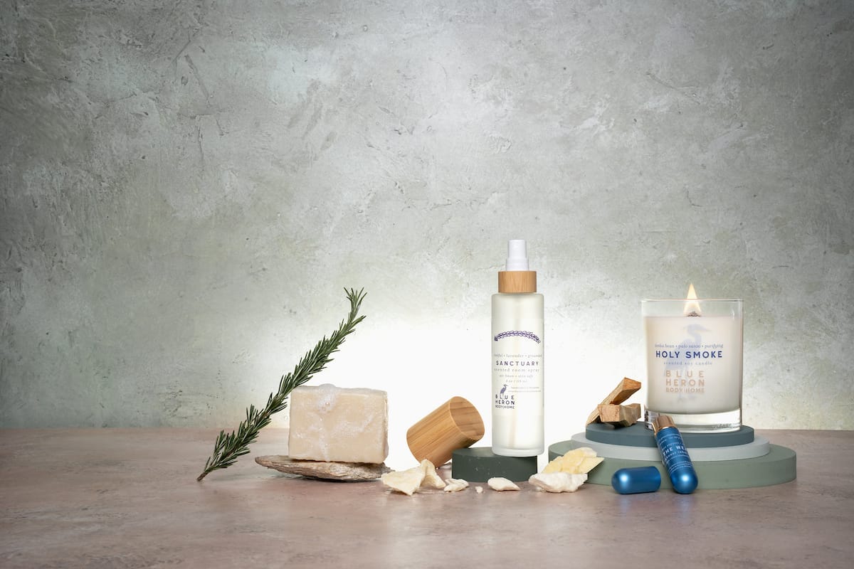 Collection of wellness products including a candle, bottle, and stones on a wooden surface with a concrete wall background.