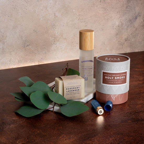 Palm-free earth soap, room spray, candle, and inhaler on a wooden surface with a plant.